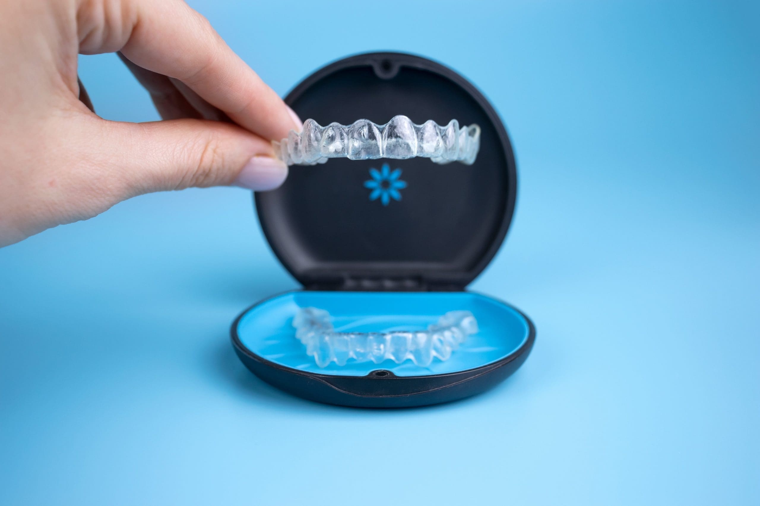 Hand holding up Invisalign aligners from it's case.